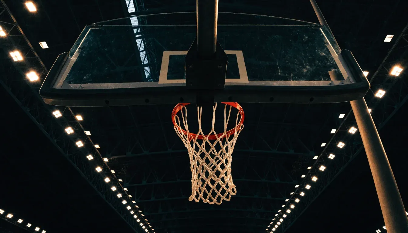 Ein Basketballkorb von unten gesehen, darüber eine Hallendecke mit Scheinwerfern und Stahlträgern.