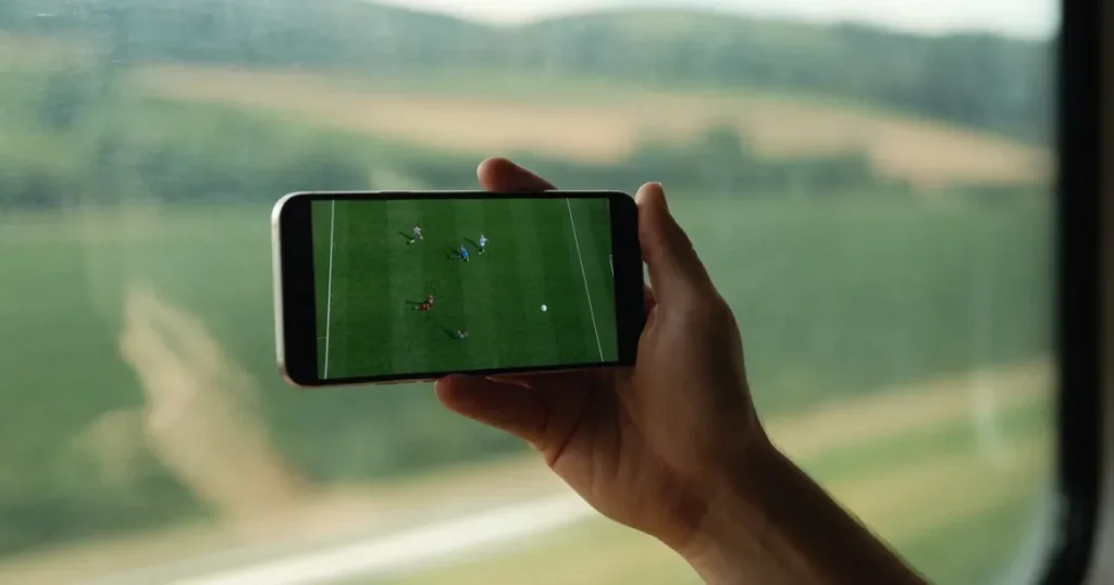 Eine Hand hält ein Smartphone mit schwarzem Bildschirm vor einem Zugfenster, draussen ziehen Hügel und Wiesen vorbei.